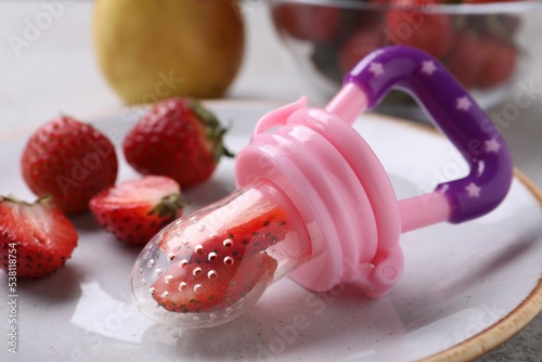 Plastic nibbler with fresh strawberries on plate, closeup. Baby feeder photo