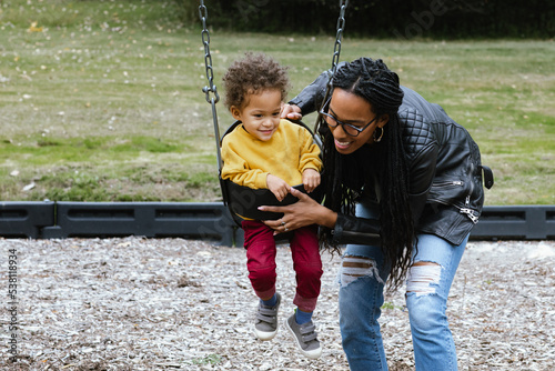 Mother pushing child on swing at park 