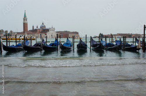 Le onde dell'acqua alta superano le gondole e invadono la riva di fronte a Piazza San Marco a Venezia photo