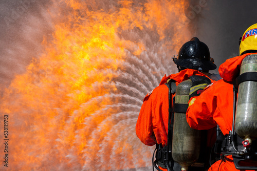 Asian firefighter on duty firefighting, Asian fireman spraying high pressure water, Fireman in fire fighting equipment uniform spray water from hose for fire fighting.