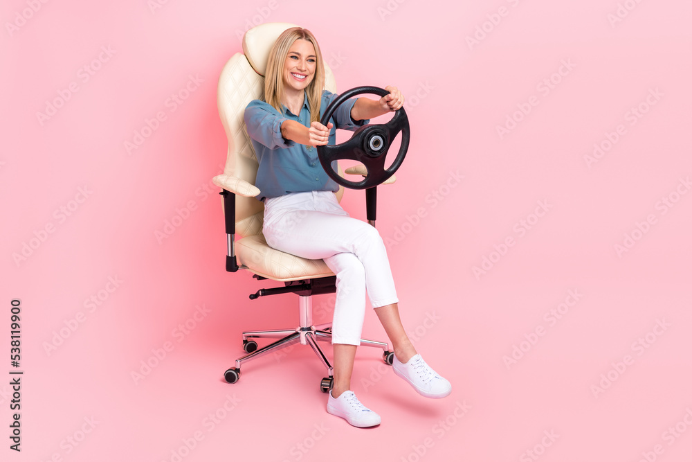 Fototapeta premium Full length photo of cheerful nice lady sitting chair arms hold wheel isolated on pink color background