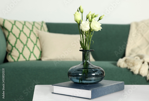 Beautiful eustoma flowers in vase and book on white wooden table indoors