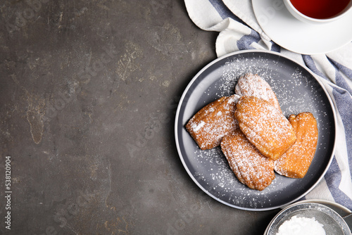 Delicious madeleine cakes with powdered sugar and tea on grey table, flat lay. Space for text photo