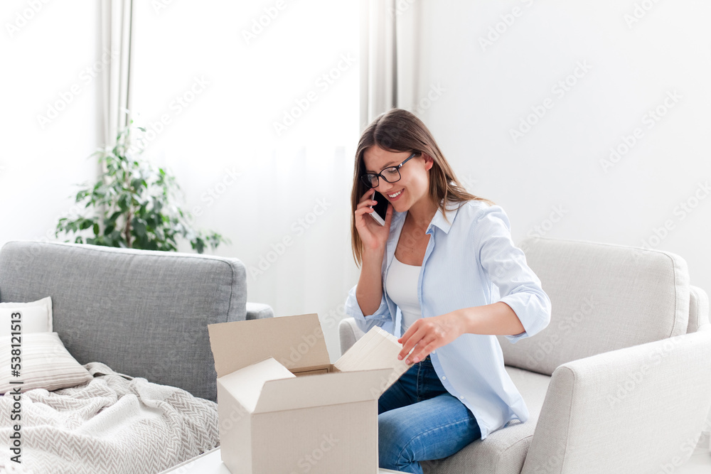 Happy woman packing order and calling by phone. Home delivery service. Girl receiving parcel, getting gift in box. Holiday shopping online. Lifestyle moment. Supporting small local business Happy woman packing order and calling by phone. Home delivery service. Girl receiving parcel, getting gift in box. Holiday shopping online. Lifestyle moment. Supporting small local business