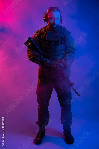 soldier in the studio on a blue background. a man in military uniform with a rifle or machine gun in colored light and smoke. military or airball player. blur © Ольга Новицкая