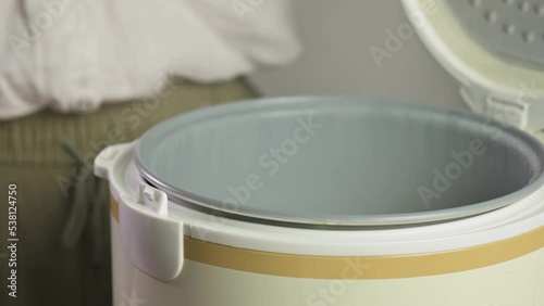 Hand opening rice cooker with steam coming out of cooked rice