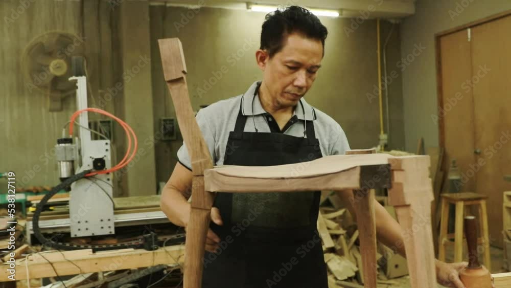 Senior asian carpenter works with wooden hammers to meticulously assemble wooden chairs and furniture in a wood factory. Senior asian carpenter works with wooden hammers to meticulously assemble wooden chairs and furniture in a wood factory.