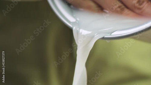 Washing raw white Thai jasmine long grain rice pouring out white cloudy starchy water liquid from the bowl.