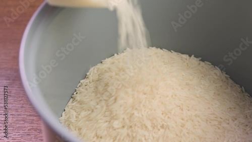 Pouring raw white Thai jasmine long grain rice into a bowl of rice cooker.