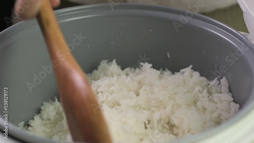 wooden spoon stir cooked white Thai jasmine long grain rice in a rice cooker bowl close up slow motion.