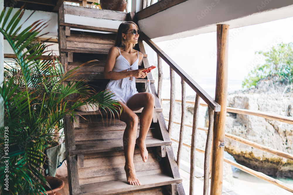 Smiling young woman sitting on stairs with smartphone on villa Smiling young woman sitting on stairs with smartphone on villa