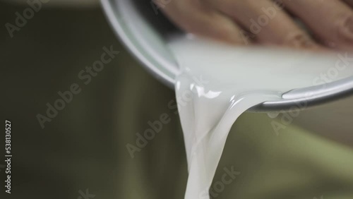 Washing raw white Thai jasmine long grain rice pouring out white cloudy starchy water liquid from the bowl in slow motion.