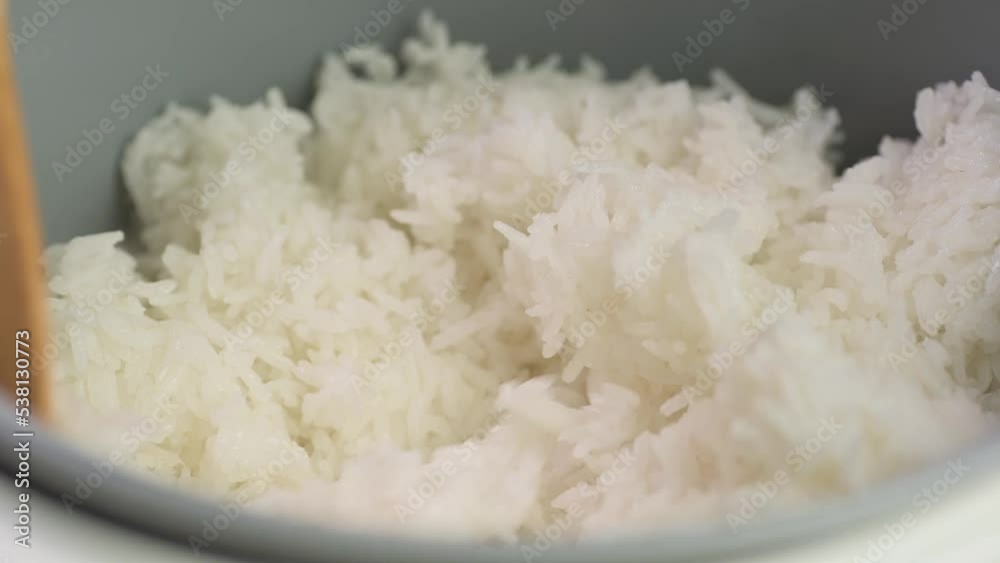 wooden spoon stir cooked white Thai jasmine long grain rice in a rice cooker bowl close up slow motion.