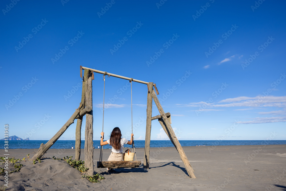 Rear view of young woman sit on swing at sand beach Rear view of young woman sit on swing at sand beach