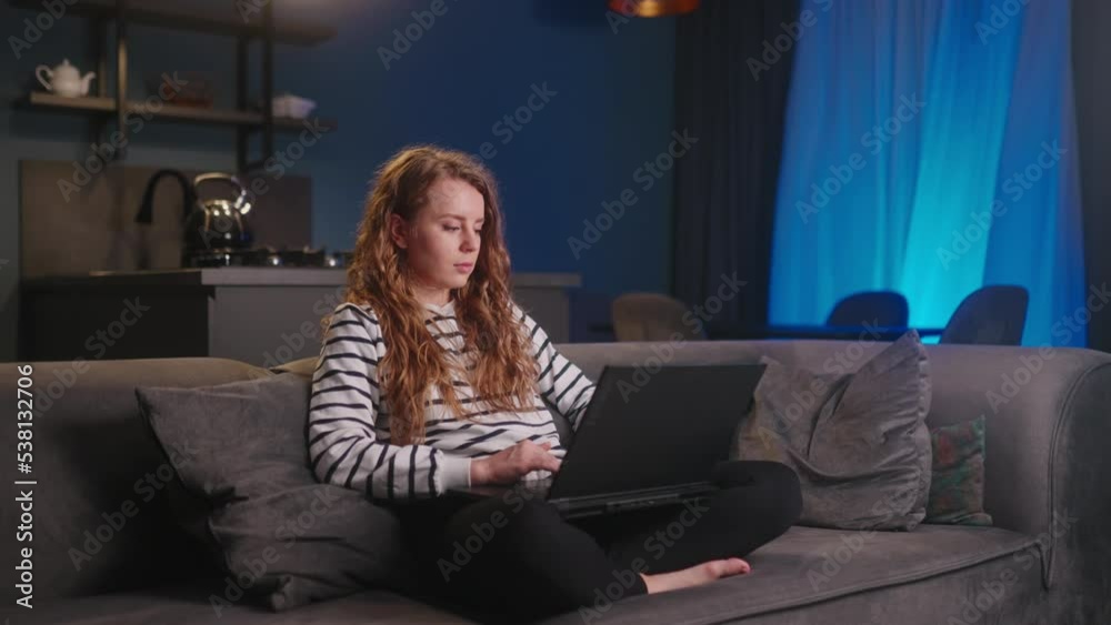 Young freelancer woman working with laptop from home sitting on sofa in living room at night. Female typing on keyboard for remote job project. Focused girl using computer for online study, homework. Young freelancer woman working with laptop from home sitting on sofa in living room at night. Female typing on keyboard for remote job project. Focused girl using computer for online study, homework.