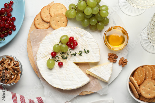 Brie cheese served with honey, berries and crackers on white table, flat lay