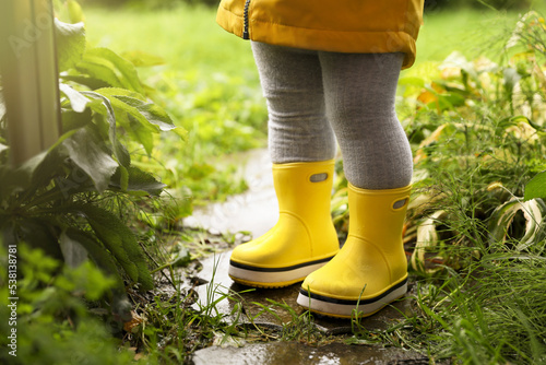 Little girl wearing rubber boots standing in puddle outdoors, closeup