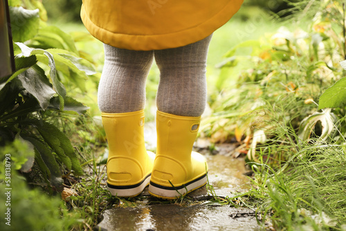 Little girl wearing rubber boots standing in puddle outdoors, closeup