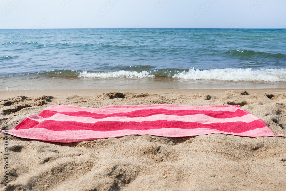 Pink striped towel on beach sand near sea Pink striped towel on beach sand near sea