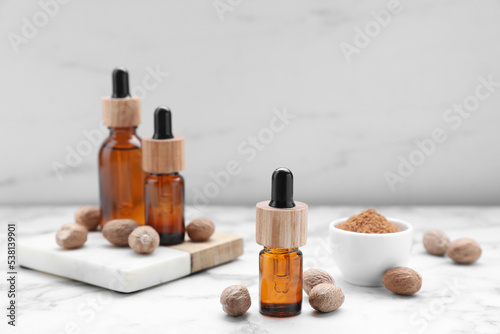Bottles of nutmeg oil and nuts on white marble table