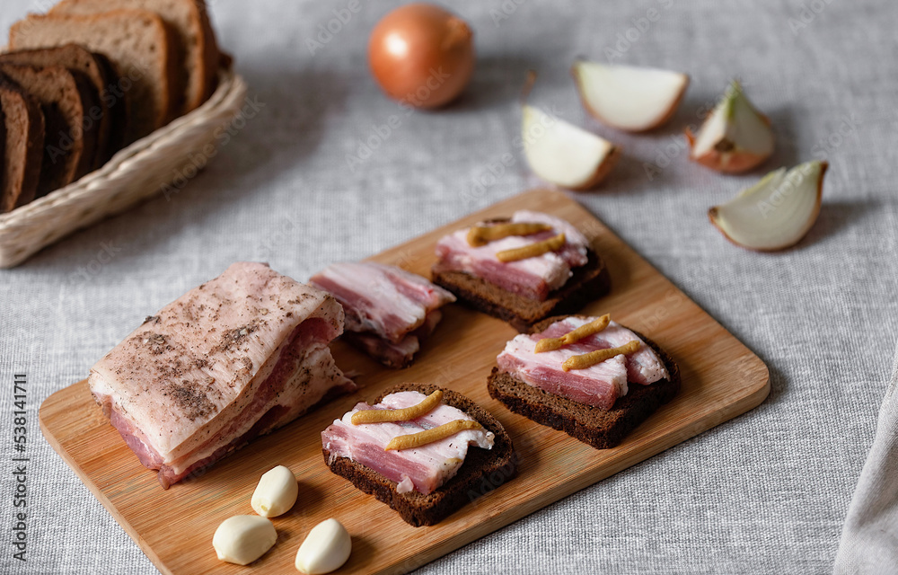 rustic natural food, on a linen tablecloth a wooden board, on it are ready-made sandwiches from black rye bread and lard with mustard and boiled eggs.