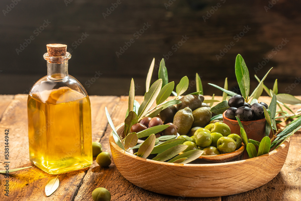 olives berries in wood bowls and pressed oil in glass bottles on a wooden background. place for text
