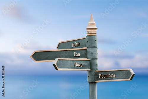 faith can move mountains four word quote written on fancy steel signpost outdoors by the sea. Soft Blue ocean bokeh background.