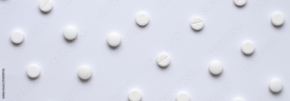Medical background of many tablets or pills on a white background. Medical pharmacy and medicine concept with copy space. Horizontal banner on a medical theme. A scattering of white pills.