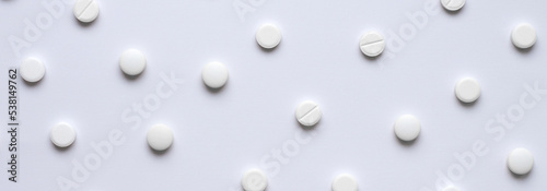 Medical background of many tablets or pills on a white background. Medical pharmacy and medicine concept with copy space. Horizontal banner on a medical theme. A scattering of white pills.