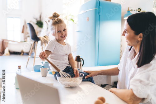 Little girl preparing dough with mother at kitchen counter