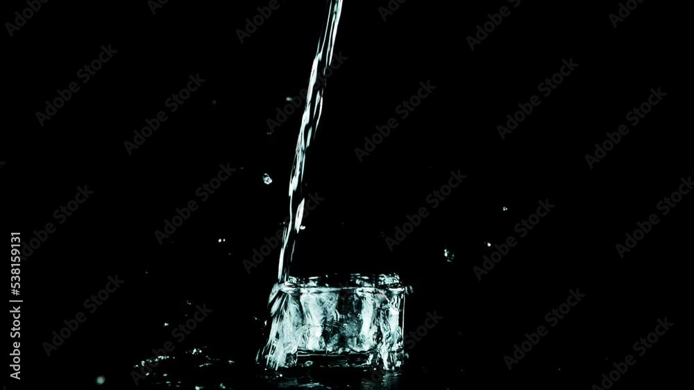 A jet of water falls into a glass container on a black background and creates a splash of water. Slow motion. A jet of water falls into a glass container on a black background and creates a splash of water. Slow motion.