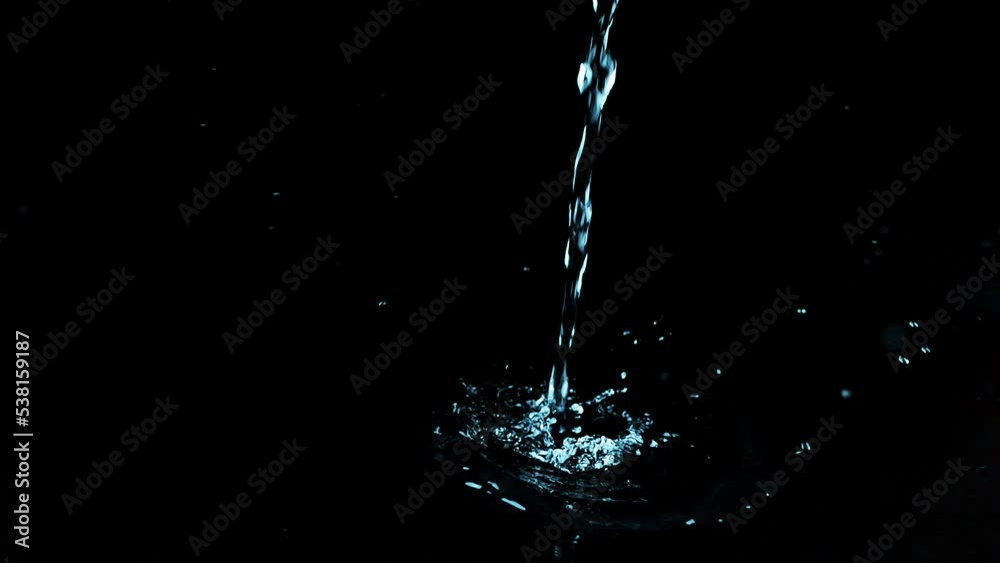 A stream of water falls and creates a splash on a black background. Slow motion.