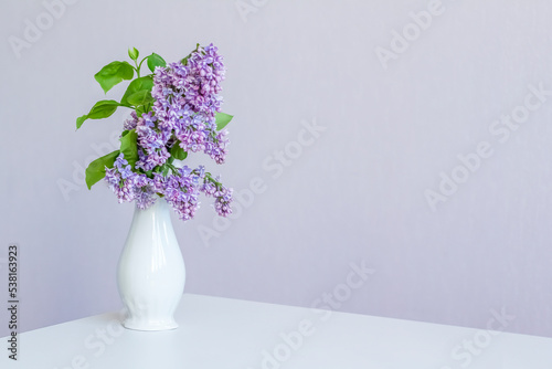 Bouquet of lilacs in a white vase on a light background. Copy space