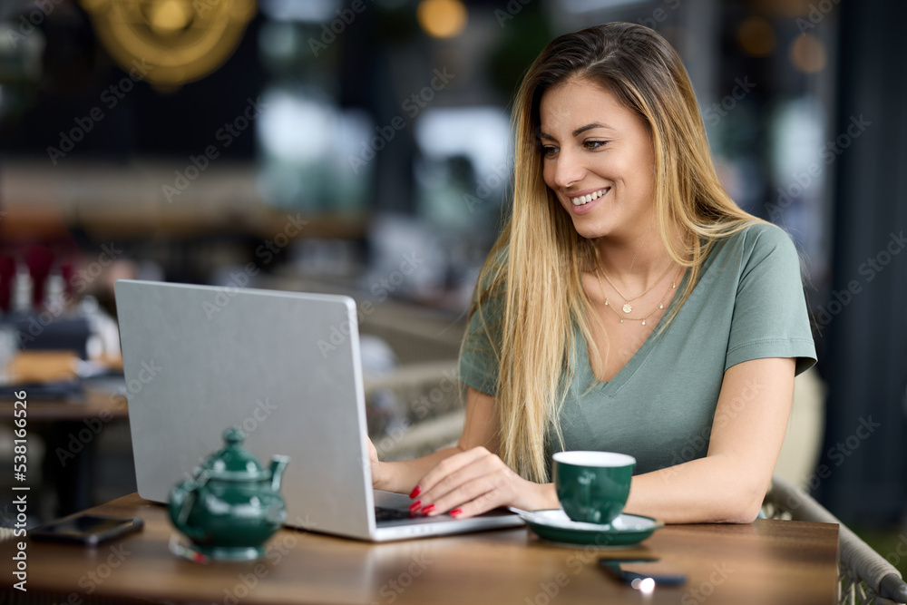 A smiling freelancer sits in a cafe and typing on a laptop while looking at monitor. A smiling freelancer sits in a cafe and typing on a laptop while looking at monitor.