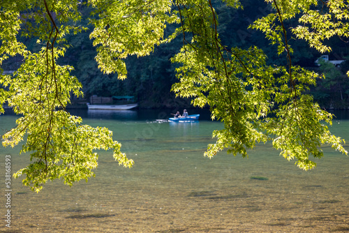 View through the trees of a calm cozy river in Japan, where a rowboat is just in the distance. 