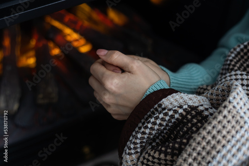 Woman rubbing hands and heating in front a fire place at home in winter.