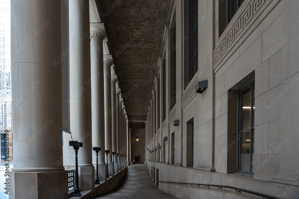 Diminishing perspective of exterior dark hallway with columns on one side and wall with windows on the other