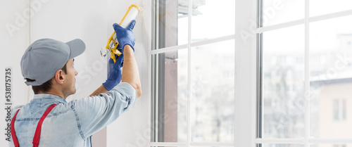 Tableau sur toile Construction worker sealing window with caulk indoors