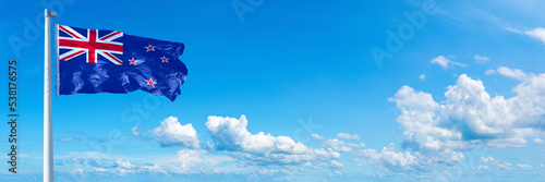 New Zealand flag waving on a blue sky in beautiful clouds - Horizontal banner