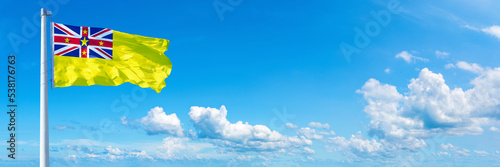 Niue, flag waving on a blue sky in beautiful clouds - Horizontal banner