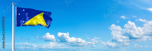 Tokelau flag waving on a blue sky in beautiful clouds - Horizontal banner