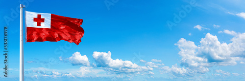 Tonga flag waving on a blue sky in beautiful clouds - Horizontal banner