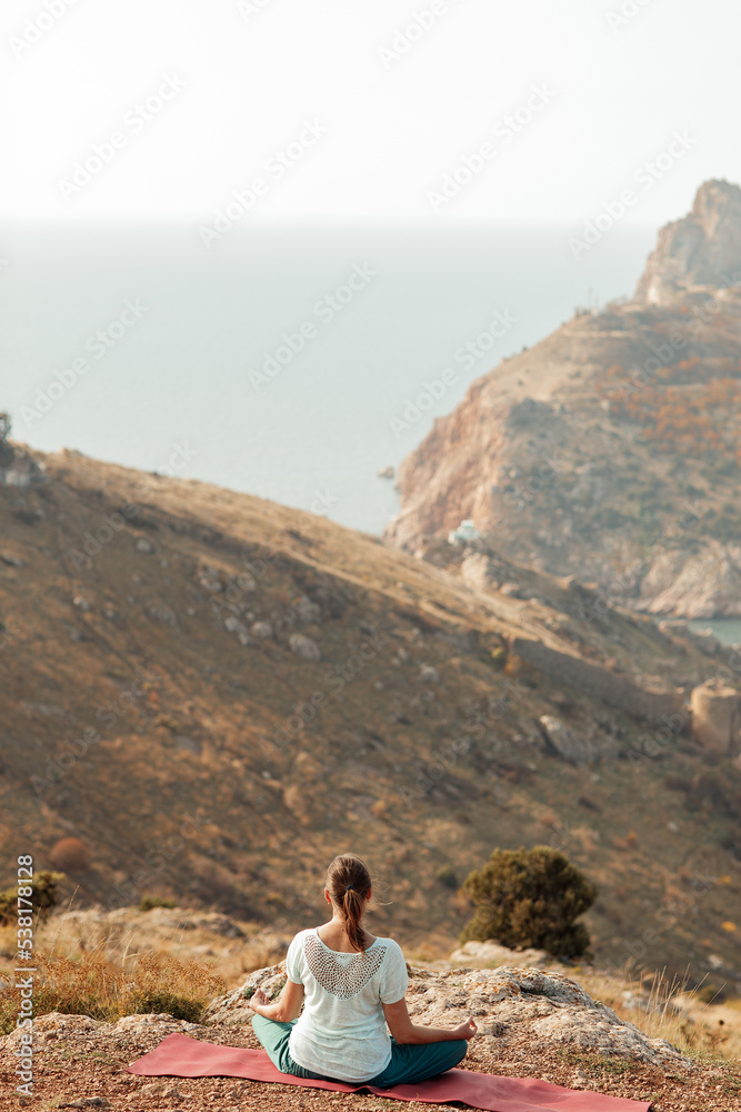 An elderly woman practices yoga on a mountain overlooking the sea