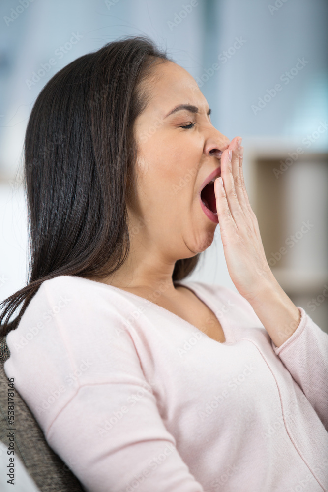 young woman yawning and stretching on sofa in living room