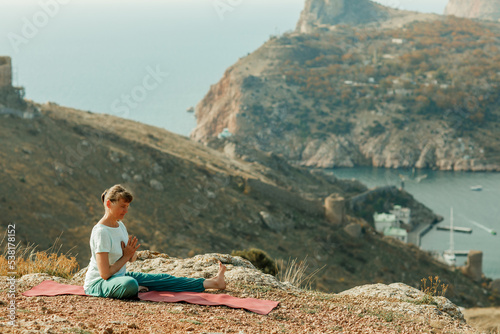 An elderly woman practices yoga on a mountain overlooking the sea