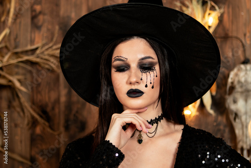 young girl in the image of a witch, wearing a black hat and a black dress with a make-up