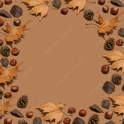 Creative layout of dry autumn leaves, pine cones and chestnut on brown background. Flat lay. Season concept. Warm tones.