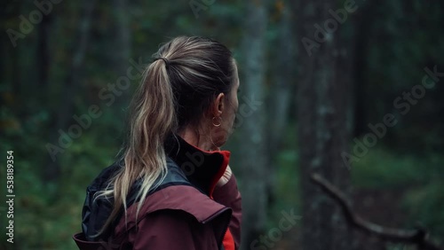 Blonde girl looks around in the forest. Puzzled hiker is worried about the coming twilight. Lost in the woods. Fear, feeling lost, lost the path. Young woman thinks what to do and where to go..