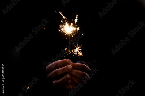 Human people hands holding fire sparkler in black background. Concept of holiday and fun. Hope and future with copy space. Close up. Party event and loneliness. One woman celebrate alone in the dark
