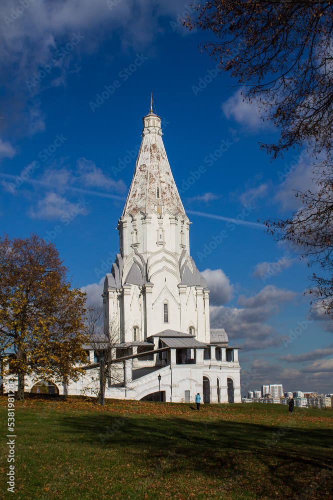 MOSCOW, RUSSIA - OCTOBER, 15, 2022: the ancient white-stone bell tower of St. George's Church against the blue sky with clouds in Kolomenskoye Park on a sunny autumn day